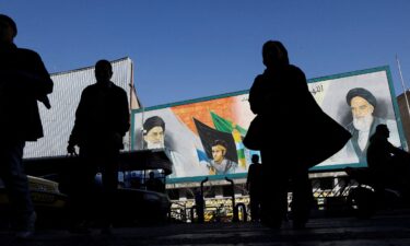 People walk near a mural featuring images of Iran's Supreme Leader Ayatollah Ali Khamenei and leader of Iran's 1979 Islamic Revolution Ayatollah Ruhollah Khomeini