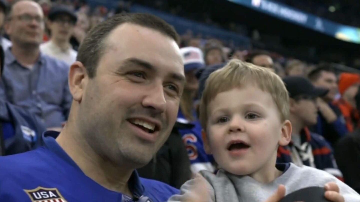 A man and his son smile at the camera during a hockey game