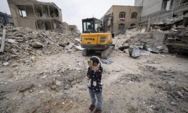 A young Iranian girl closes her eyes near a loader working on the ruins of buildings destroyed during a military campaign in Tehran