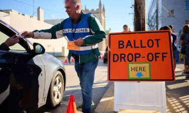 An official ballot collector for the Cuyahoga County Board of Elections gives a voter their "I Voted" sticker after depositing their mail-in ballots into a collection box in Cleveland