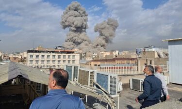 People watch as smoke rises after an explosion in Tehran