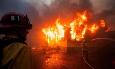 The light of a fire fighting helicopter illuminates a smouldering hillside as the Palisades fire grows near the Mandeville Canyon neighborhood and Encino