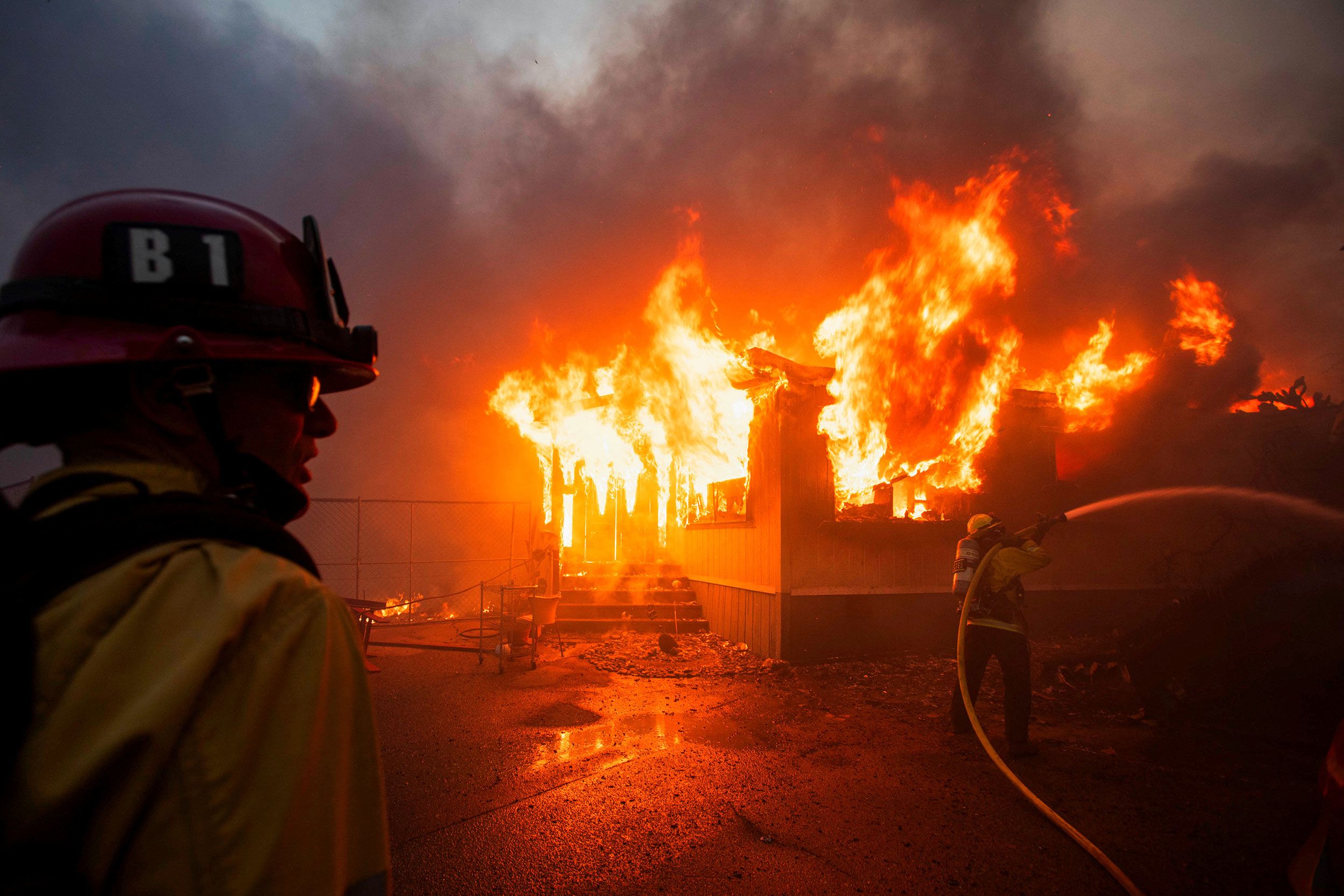 <i>Patrick T. Fallon/AFP/Getty Images via CNN Newsource</i><br/>The light of a fire fighting helicopter illuminates a smouldering hillside as the Palisades fire grows near the Mandeville Canyon neighborhood and Encino