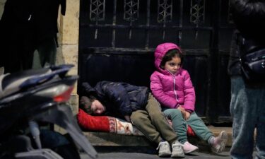 Children sit on a sidewalk as displaced families fleeing Israeli strikes in southern Lebanon arrive in the southern port city of Sidon