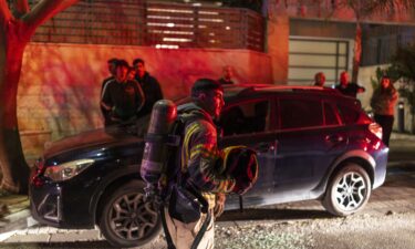 A firefighter holds a helmet as he operates outside a building hit by a projectile in a city in outskirts of Tel-Aviv