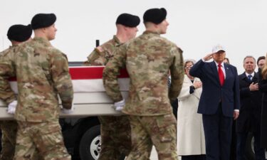 President Donald Trump stands as members of military carry a transfer case during a dignified transfer of the remains of six U.S. Army service members