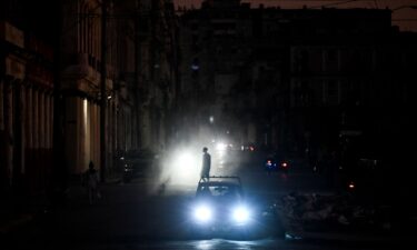 A man walks while cars cruise along a street during a blackout in Havana on March 16.