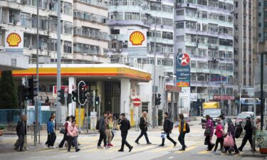 Pedestrians walk through a zebra crossing in front of the gas stations logos from the energy and petrochemical company