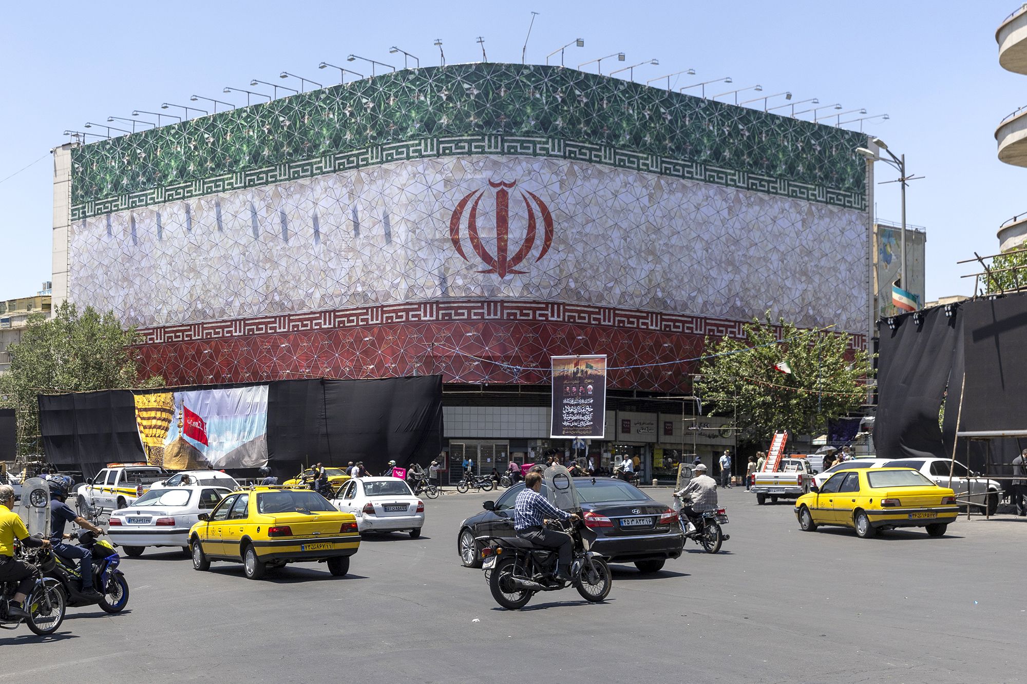 Cars and monocycles are seen traveling in front of a billboard displaying the Iranian flag on in Tehran, Iran, on Monday.