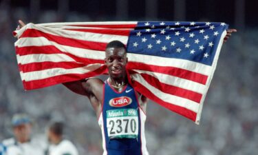 Michael Johnson holds up the American flag behind him on the track at the 1996 Atlanta Summer Olympics.