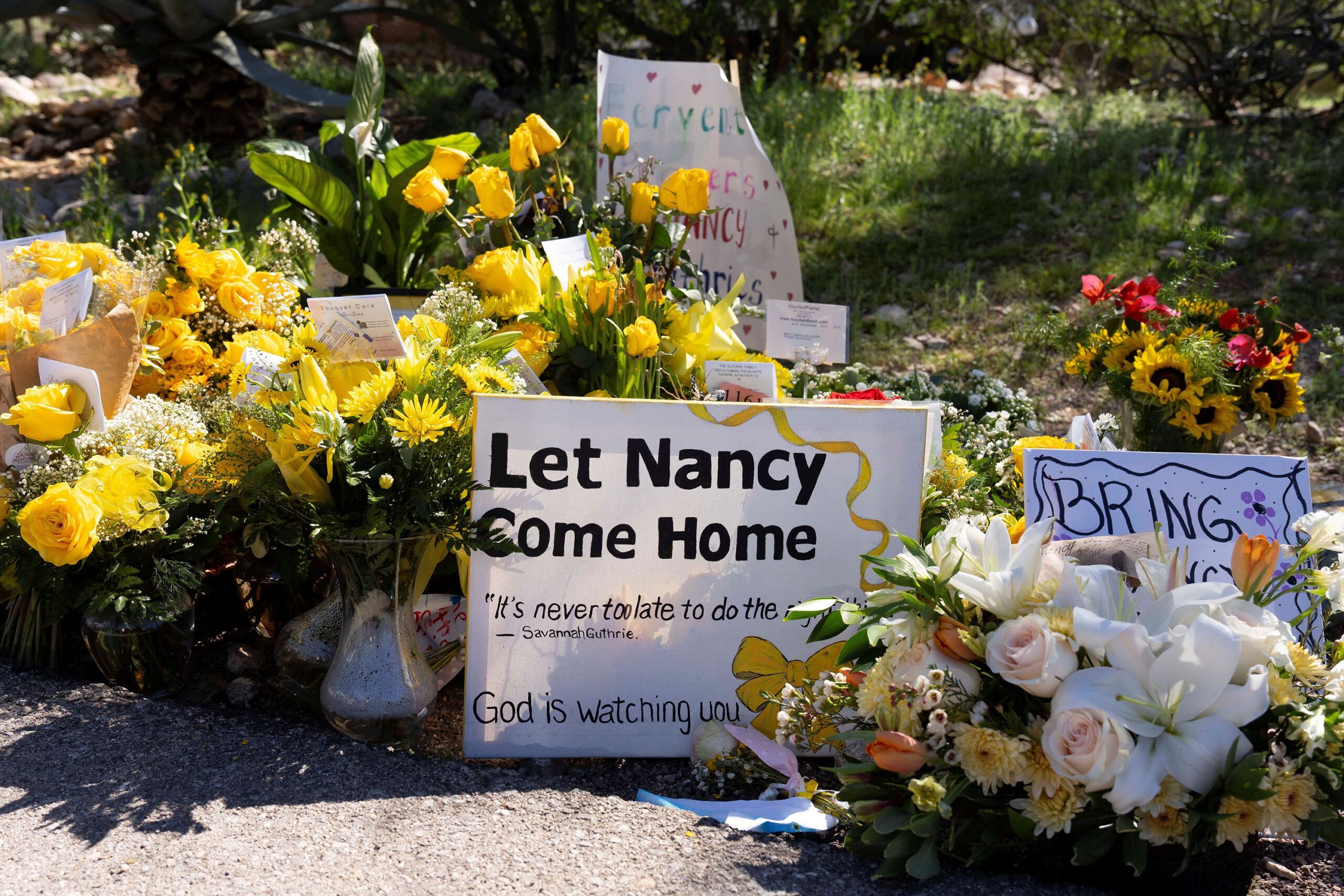 <i>Rebecca Noble/Reuters via CNN Newsource</i><br/>A sign reads stands amid yellow flowers left at the house of Nancy Guthrie
