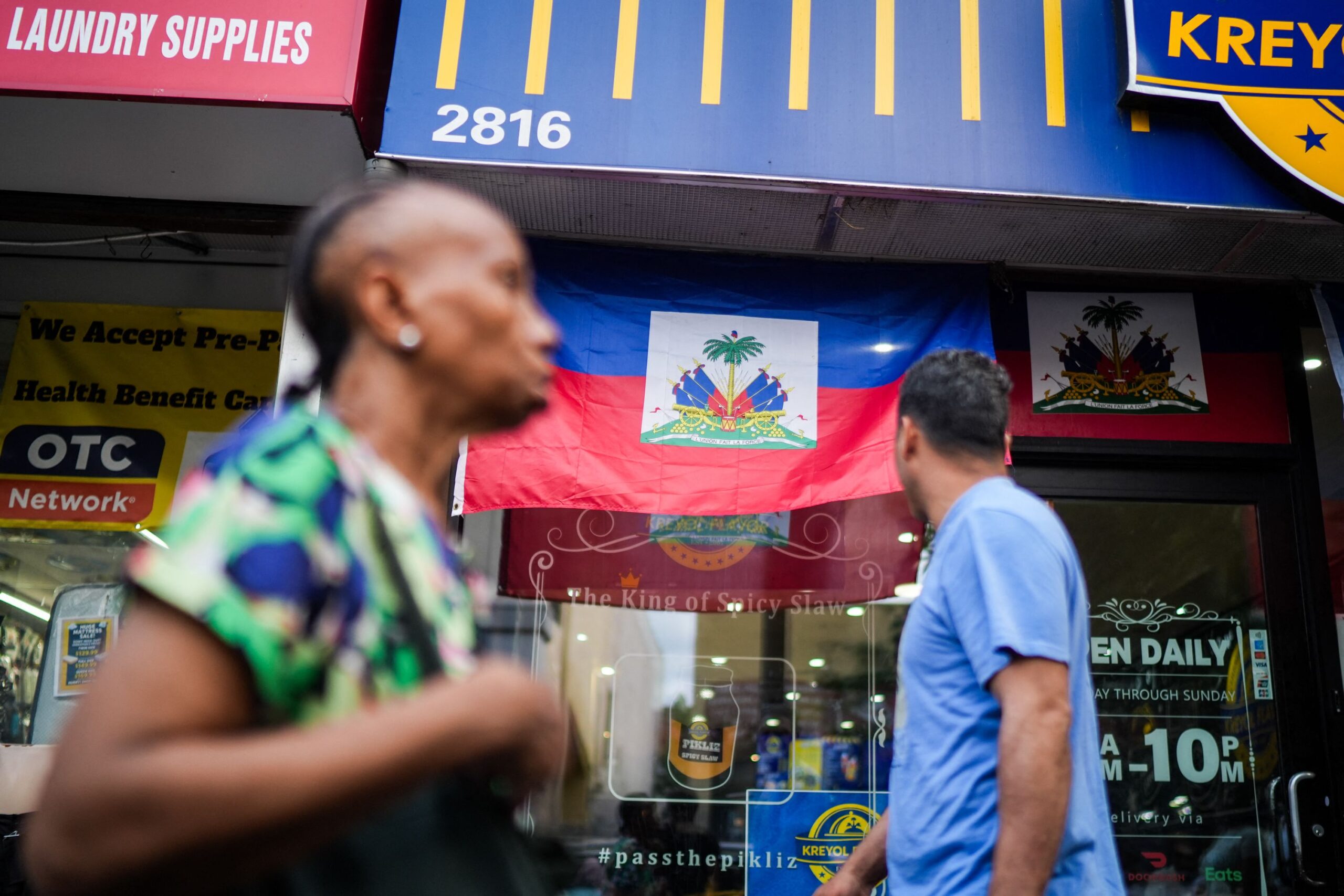<i>Ryan Murphy/AFP/Getty Images via CNN Newsource</i><br/>People walk past a restaurant displaying Haitian flags in the Little Haiti neighborhood of Brooklyn