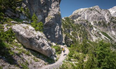 A hiker descends from the Valbona Pass along the Peaks of the Balkans Trail. The Peaks of the Balkans hiking trail is a challenging yet incredibly rewarding long-distance trek that winds through the remote and spectacular Accursed Mountains of Albania