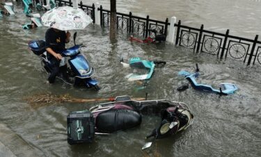 A flooded street is filled with fallen scooters during heavy rain brought by Typhoon Dolphin after it weakened into a tropical storm