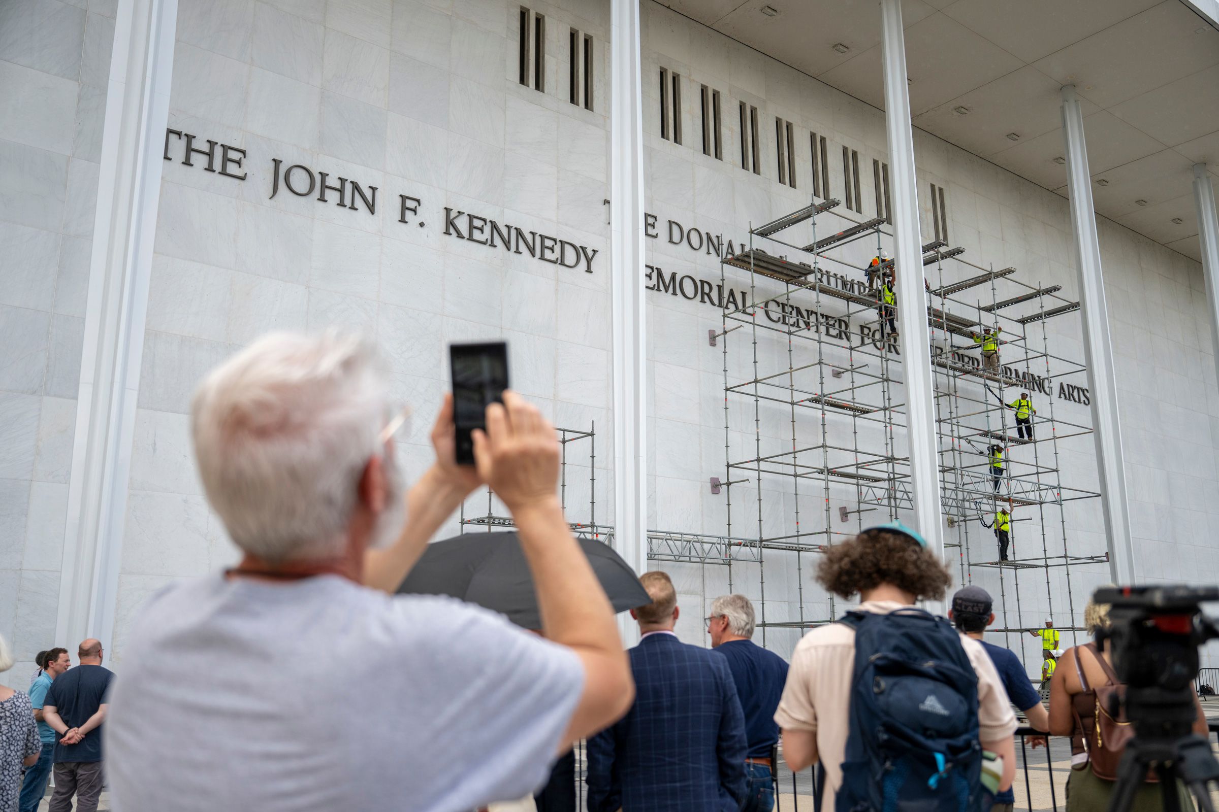 <i>Daniel Heuer/Bloomberg/Getty Images via CNN Newsource</i><br/>People stop to watch workers erect scaffolding at the Kennedy Center in Washington