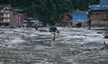 People walk on a suspension bridge to cross the flooded Trishuli River in Bhaise