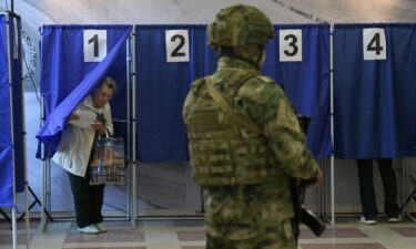 People vote in Russia's parliamentary election as a Russian serviceman secures a polling station in Donetsk