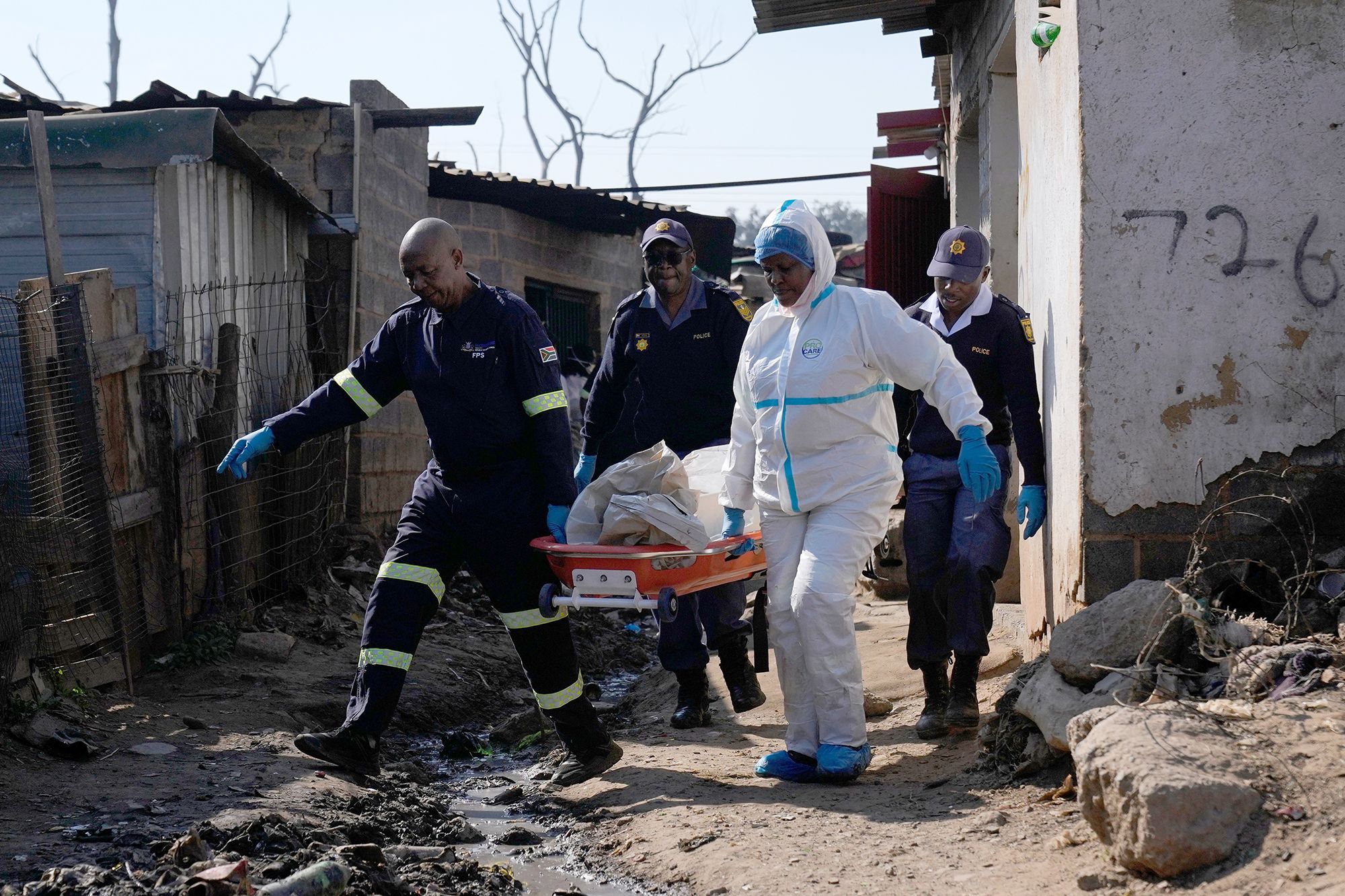 <i>Themba Hadebe/AP via CNN Newsource</i><br/>Police officers carry the body of a person on a stretcher after a mass shooting at an informal settlement in the Cleveland suburb of Johannesburg