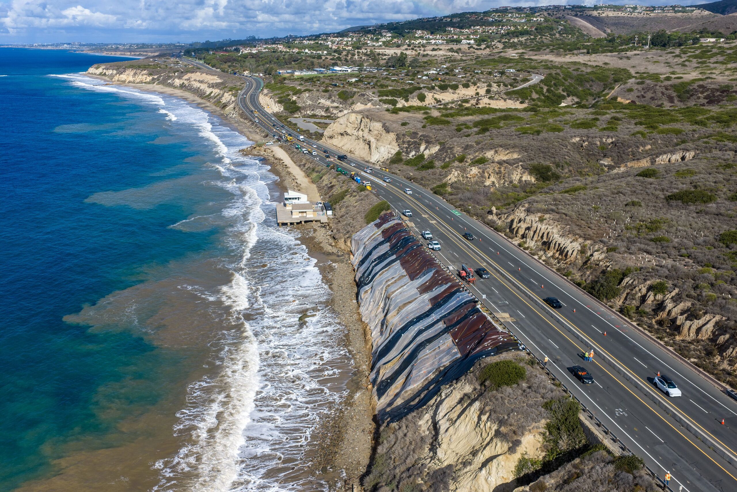 <i>Allen J. Schaben/Los Angeles Times/Getty Images via CNN Newsource</i><br/>Protective plastic sheeting covers a long crack in a hillside alongside the southbound lanes of the Pacific Coast Highway at Moro Beach on Thursday